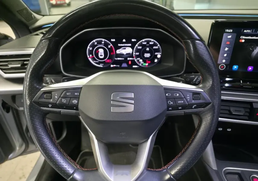 Vue rapprochée du volant noir perforé avec surpiqûres rouges et tableau de bord digital du SEAT Leon Sportstourer 2022.