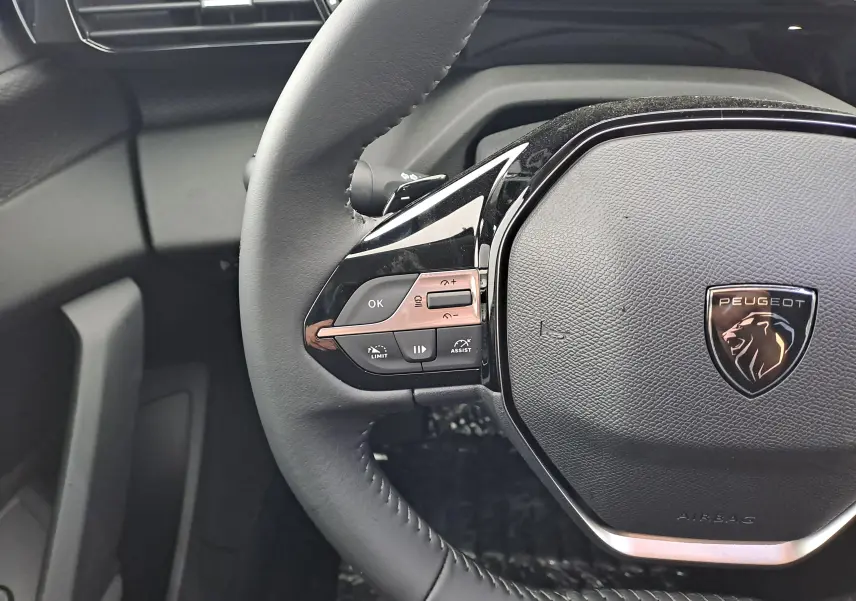 Gros plan sur le volant noir de la Peugeot 308 2025, avec commandes intégrées et logo lion chromé au centre.