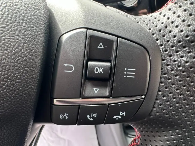 Gros plan sur les commandes multifonctions à gauche du volant perforé d’un Ford Puma 2024 Noir Agate Métallisée.