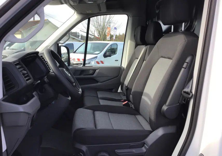 Intérieur du Volkswagen Crafter Fourgon blanc 2024, vue côté conducteur, sièges tissu gris et tableau de bord noir.