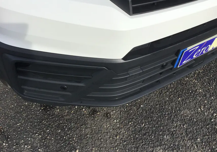 Gros plan sur le pare-chocs avant blanc du Volkswagen Crafter Fourgon 2024 avec caméra de recul intégrée.