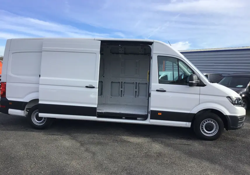 Vue latérale droite d'un Volkswagen Crafter blanc 2024 avec porte coulissante ouverte dévoilant l'espace de chargement vide.