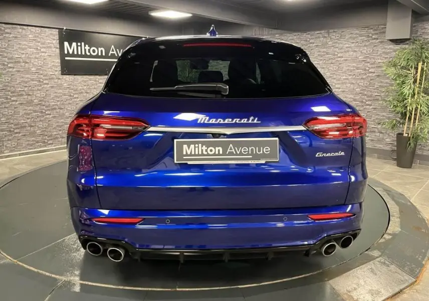 Vue arrière d'une Maserati Grecale bleu brillant avec quadruple sortie d'échappement et logo Maserati lumineux.