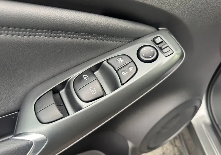 Gros plan sur les commandes de lève-vitres et rétroviseurs sur la porte côté conducteur du Nissan Juke gris squale.