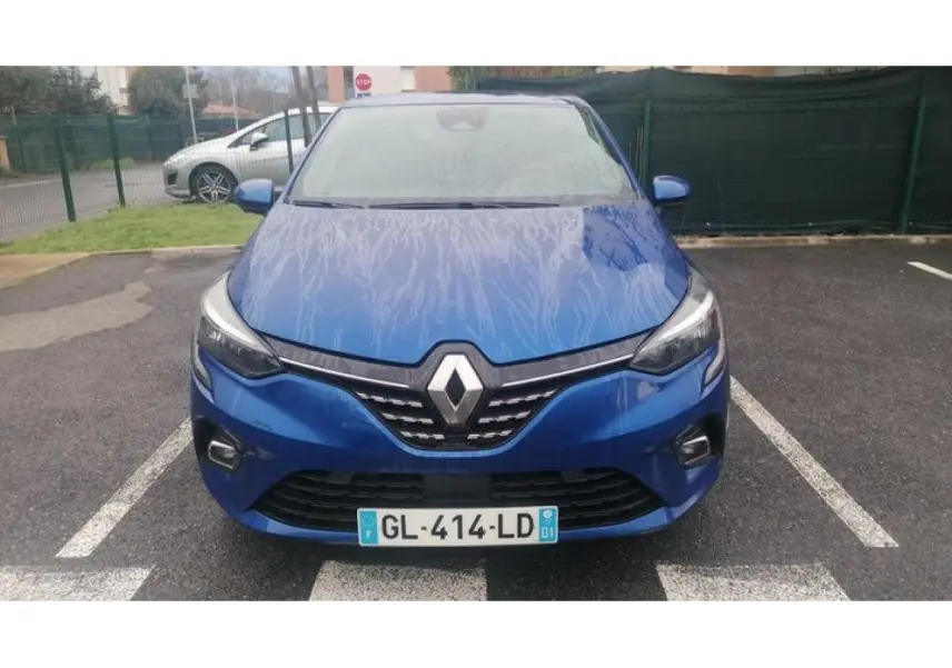 Vue avant d'une Renault Clio 2021 bleu Iron avec calandre chromée et phares LED allumés sur parking.