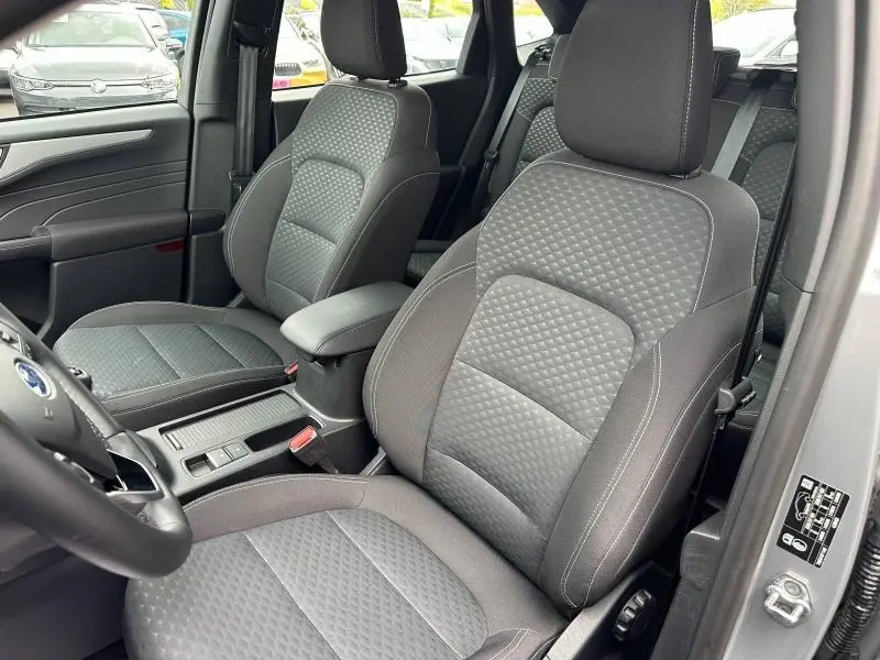 Vue intérieure côté conducteur du Ford Kuga 2024, sièges sport en tissu noir à motifs losanges, accoudoir central visible.