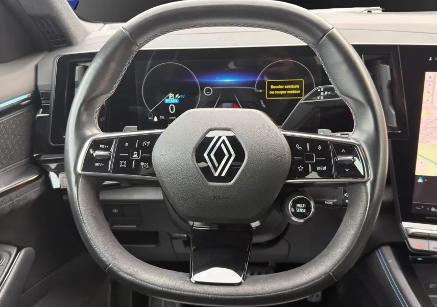 Vue frontale du volant cuir noir avec logo Renault, tableau de bord numérique et écran tactile latéral du Renault Austral gris foncé.