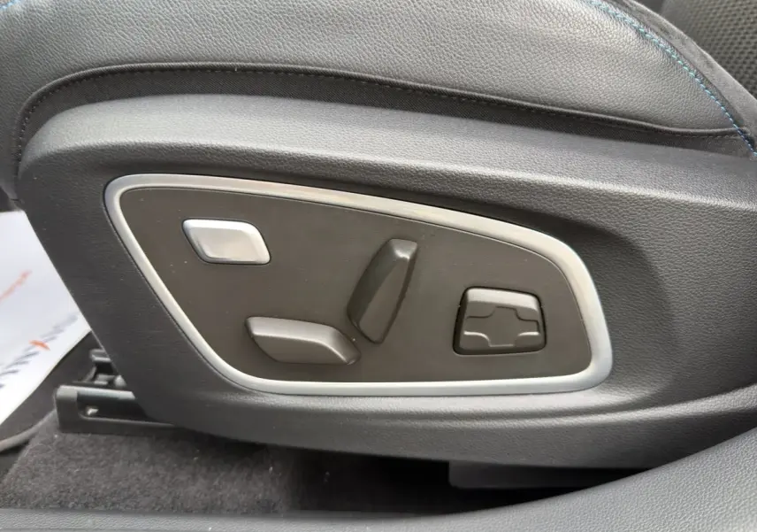 Gros plan sur les commandes de réglage électrique du siège en cuir noir avec surpiqûres bleues du Renault Austral gris foncé.