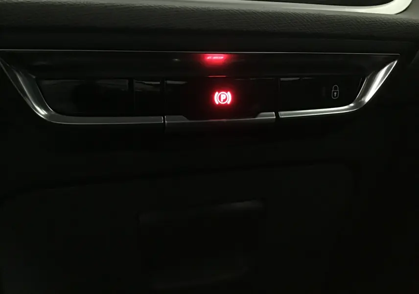 Gros plan sur le bouton de frein à main électrique rouge dans l'habitacle noir du Citroën Grand C4 Spacetourer gris Artense.