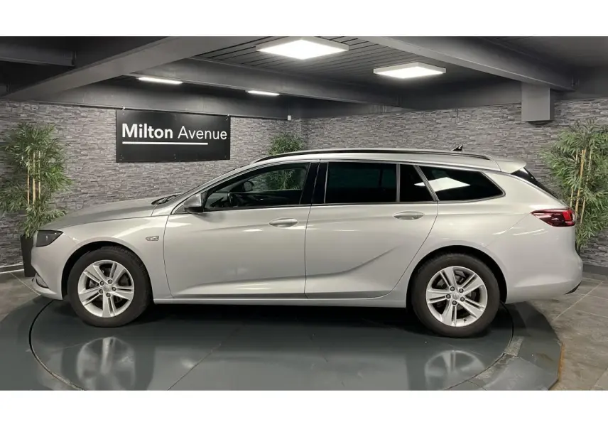 Opel Insignia Sports Tourer gris métallisé vue de profil côté gauche dans un showroom avec mur en pierre.