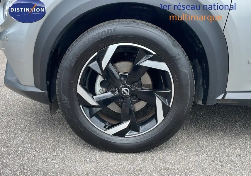 Gros plan sur la roue avant gauche du Nissan Juke gris perle métal, avec jante alliage noire et argentée au design moderne.