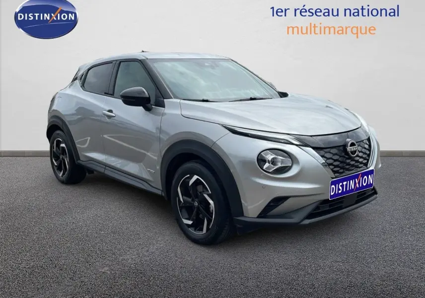 Nissan Juke Hybrid gris perle métal vu en 3/4 avant droit avec calandre noire et jantes bi-ton.