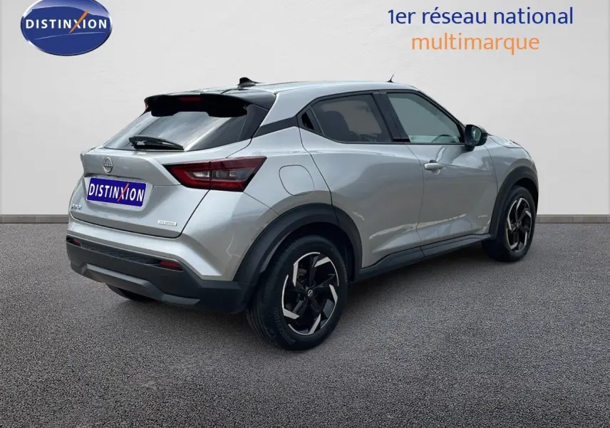 Nissan Juke Hybrid gris perle métal vu en 3/4 arrière droit, avec jantes noires et toit noir contrasté.