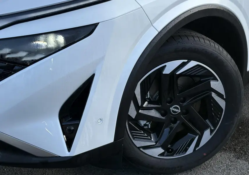 Détail de la roue avant droite et partie avant blanche nacrée du Nissan Qashqai III e-Power avec jante alliage noire et argent.