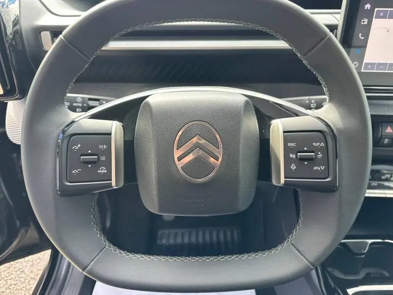 Vue rapprochée du volant noir de la Citroën C3 1.2 Turbo 100ch MAX avec commandes intégrées et logo central argenté.
