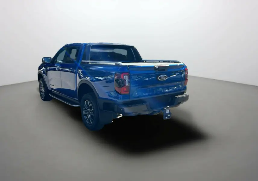 Ford Ranger 2.0 205 Wildtrak Plus bleu lightning, vue 3/4 arrière gauche avec attelage et barres de toit.