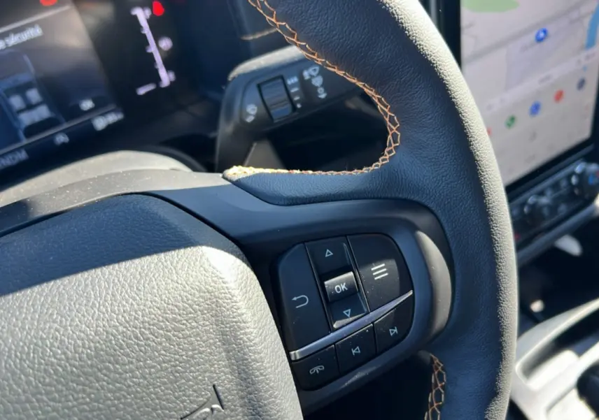 Gros plan sur le volant cuir noir avec surpiqûres marron du Ford Ranger Wildtrak 2025, tableau de bord et écran tactile en arrière-plan.