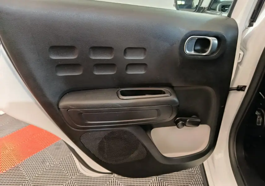 Vue rapprochée de la porte arrière droite noire avec poignée et commande de vitre manuelle d'une Citroën C3 blanche 2021.