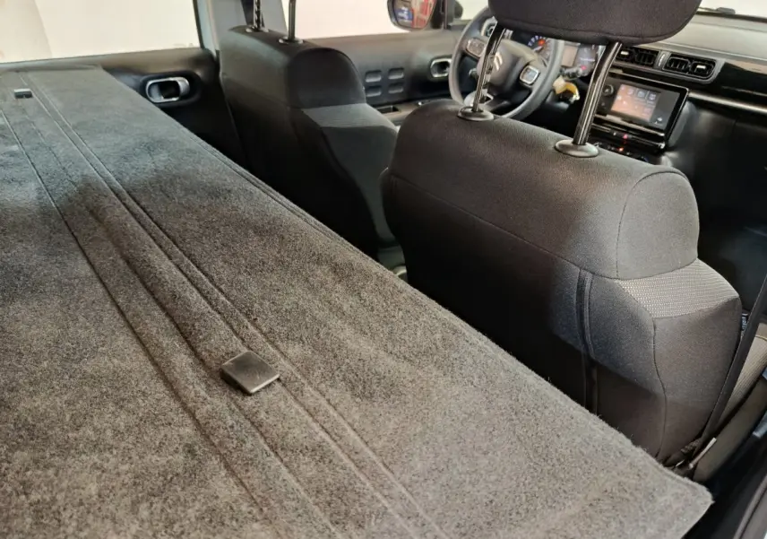 Vue intérieure arrière de la Citroën C3 blanche, banquette rabattue et tableau de bord avec écran tactile visible.