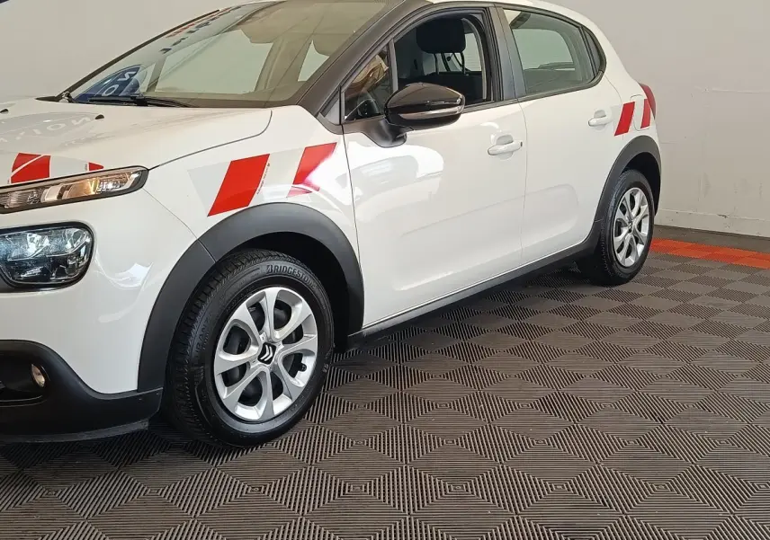 Vue de profil avant droit d'une Citroën C3 blanche 2021 avec marquages rouges sur les ailes et jantes argentées.