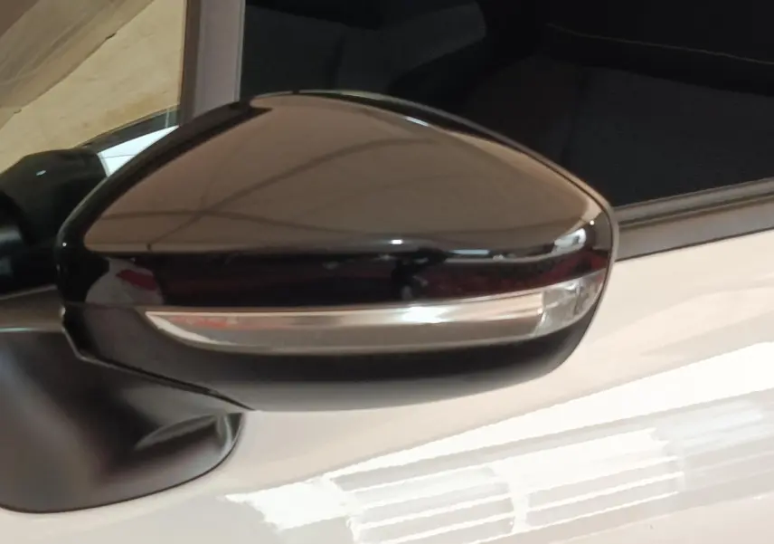 Gros plan sur le rétroviseur extérieur noir d'une Citroën C3 blanche, côté conducteur, avec clignotant intégré.