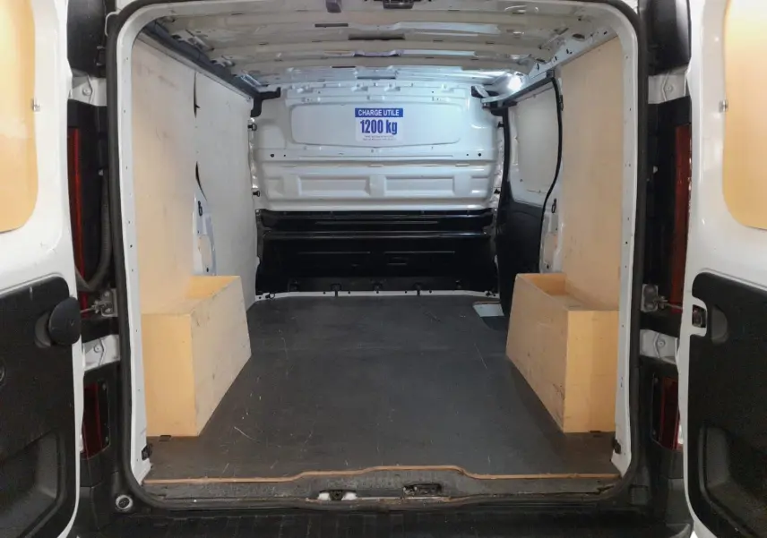Vue intérieure arrière du Renault Trafic Fourgon blanc minéral 2024, montrant l’espace de chargement vide et ses protections latérales.