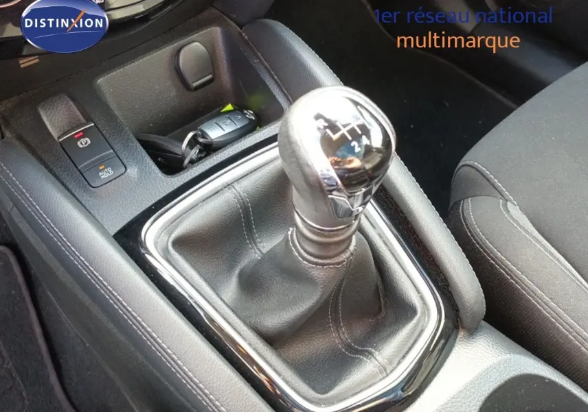 Gros plan sur le levier de vitesse manuel chromé et cuir noir du Nissan Qashqai blanc, intérieur tissu noir.