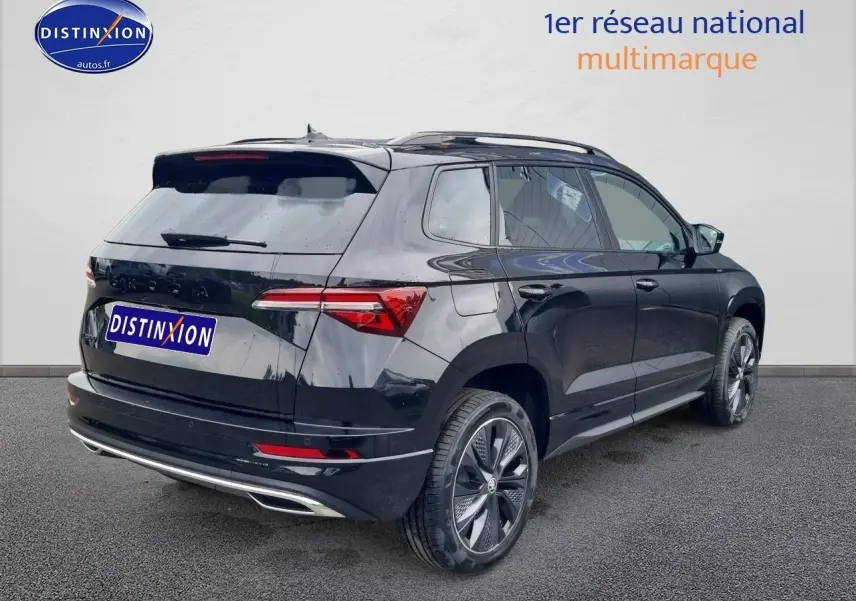 Vue 3/4 arrière droite d’un Skoda Karoq noir 2025 avec jantes alu et barres de toit visibles.