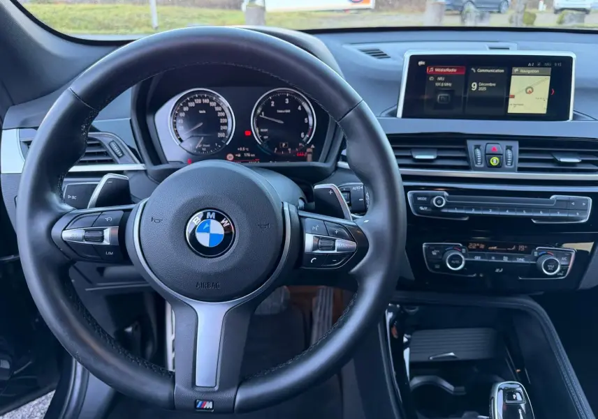 Vue intérieure centrée sur le volant cuir noir et le tableau de bord avec écran multimédia du BMW X1 noir métal 2018 M Sport.