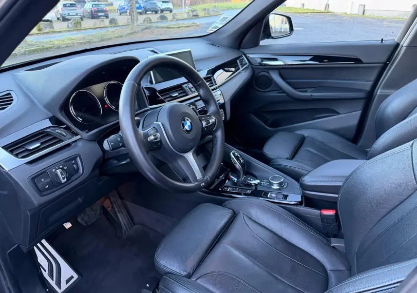 Vue intérieure côté conducteur du BMW X1 18D M Sport 2018, avec volant cuir, tableau de bord moderne et sièges en cuir noir Dakota.