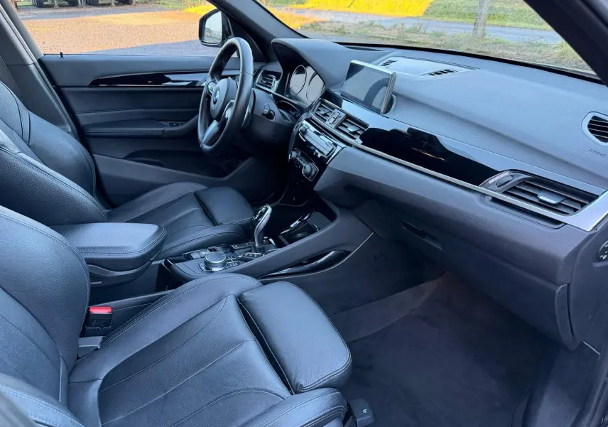 Vue intérieure côté conducteur du BMW X1 18D noir métal, avec sièges en cuir Dakota perforé et tableau de bord moderne.