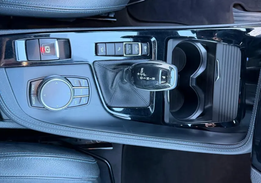 Vue plongeante sur la console centrale noire brillante du BMW X1 18D M Sport 2018 avec levier de vitesse automatique et sièges cuir noir.