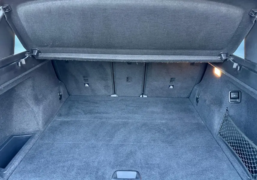 Vue intérieure du coffre spacieux et propre du BMW X1 18D noir métal, avec cache-bagages relevé et éclairage latéral allumé.