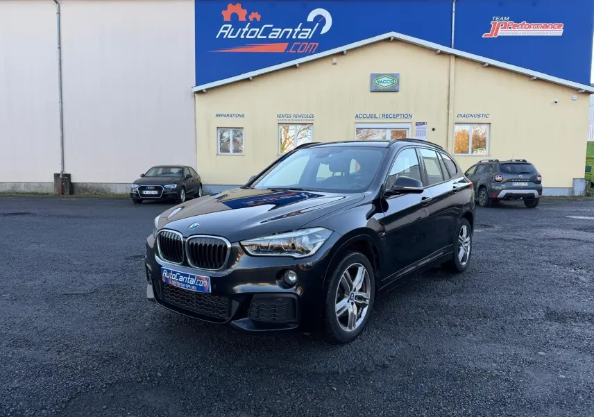 BMW X1 18D noir métal en 3/4 avant droit, finition M Sport avec calandre et jantes distinctives visibles.