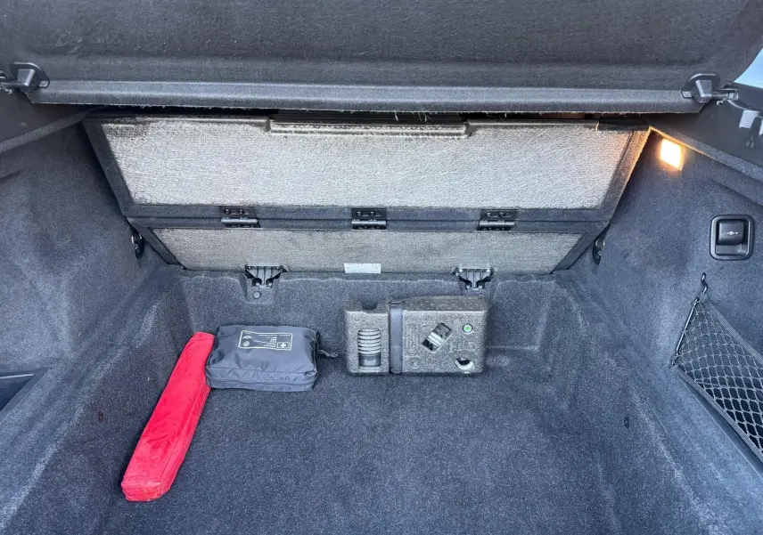 Coffre ouvert d'un BMW X1 noir métal 2018, montrant un espace de rangement avec trousse de secours et filet latéral.