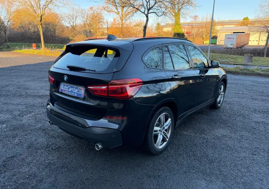 BMW X1 18D noir métal en vue 3/4 arrière droit, avec jantes alliage et double sortie d'échappement visible.