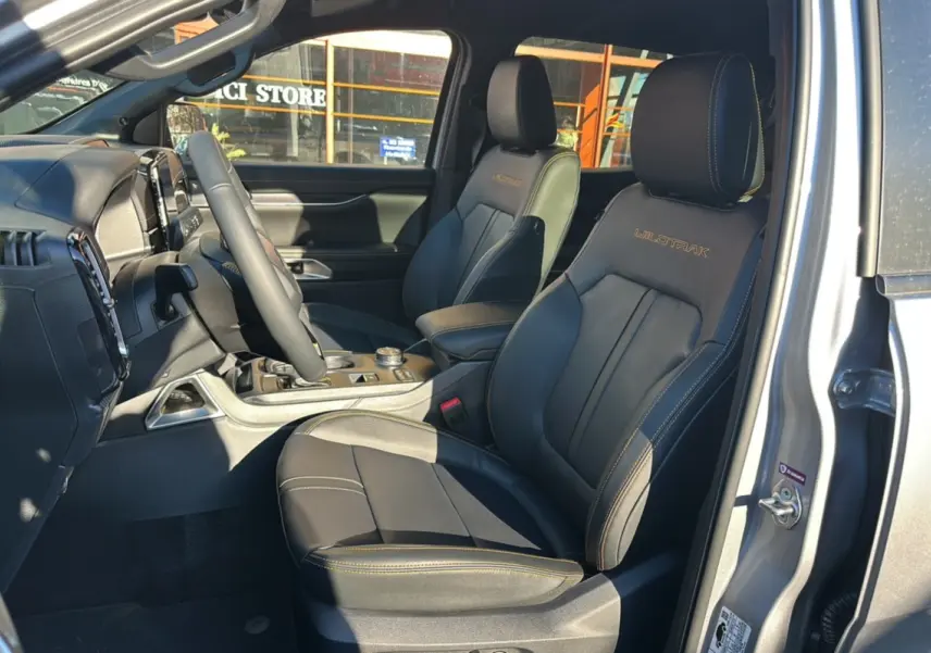 Vue intérieure côté conducteur du Ford Ranger Wildtrak 2025 gris iconic, sièges cuir noirs avec surpiqûres orange.