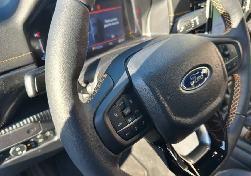 Gros plan sur le volant cuir noir avec surpiqûres orange du Ford Ranger 2025, affichage numérique en arrière-plan.