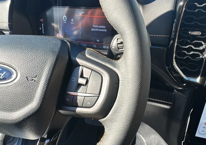 Gros plan sur le volant cuir multifonctions du Ford Ranger 2025, avec tableau de bord numérique en arrière-plan.