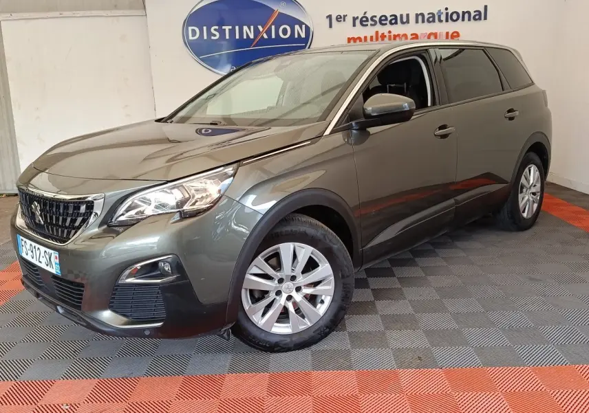 Peugeot 5008 gris foncé vue en 3/4 avant droit, avec phares allumés et jantes alliage, en intérieur showroom.