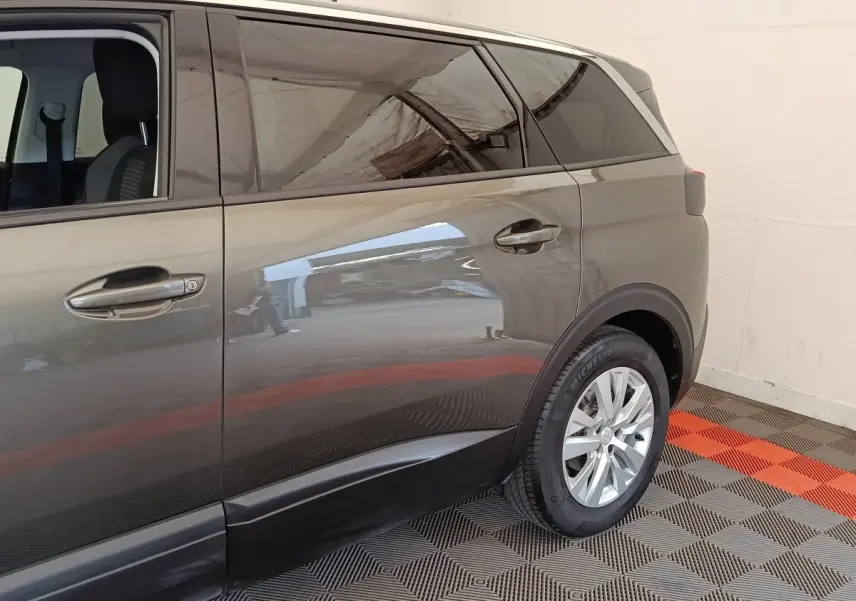Vue latérale droite du Peugeot 5008 gris foncé, mettant en valeur les portes arrière et la roue arrière sur sol à damier.