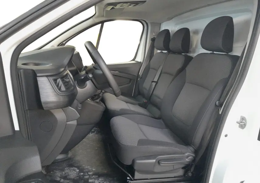 Vue intérieure côté conducteur du Renault Trafic Fourgon blanc, montrant les sièges tissu gris et le tableau de bord minimaliste.