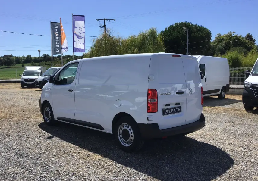 Vue 3/4 arrière droite d'un utilitaire Opel Vivaro blanc 2023 stationné sur un terrain extérieur.