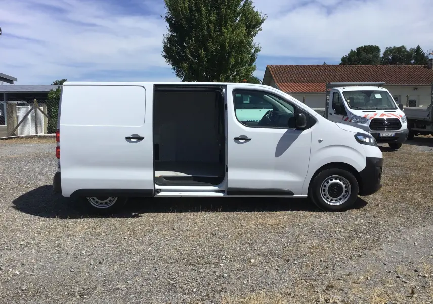 Vue de profil côté droit d'un utilitaire Opel Vivaro blanc 2023 avec porte coulissante ouverte sur un terrain extérieur.