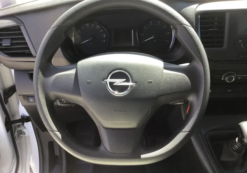 Vue rapprochée du volant noir de l'Opel Vivaro blanc 2023, avec tableau de bord et levier de vitesse manuel visibles.