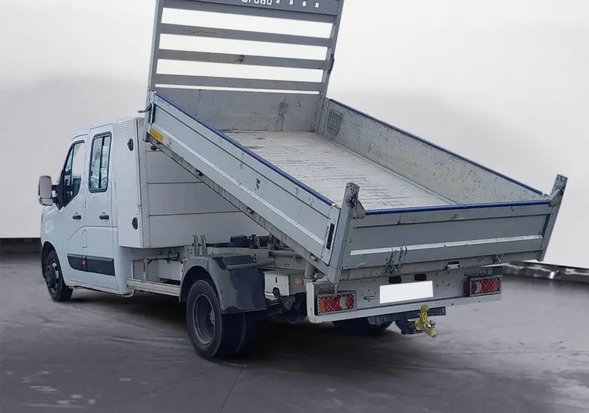 Renault Master blanc en double cabine vu 3/4 arrière avec benne basculante relevée et attelage visible.