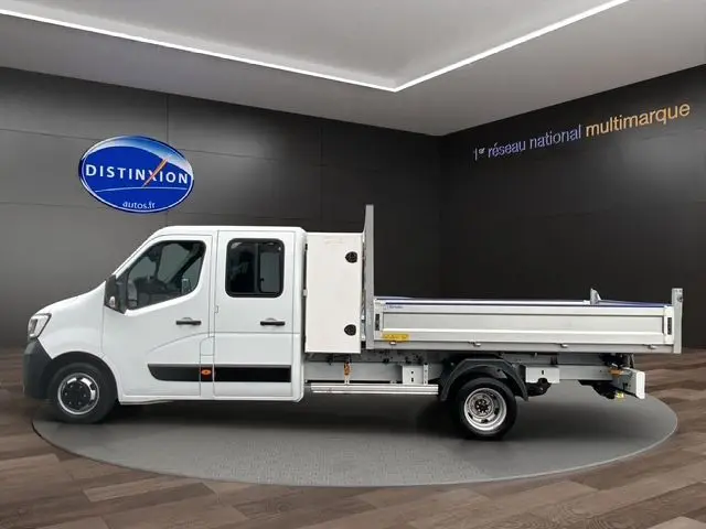 Vue latérale droite d'un Renault Master blanc double cabine avec benne et coffre, présenté en intérieur showroom.