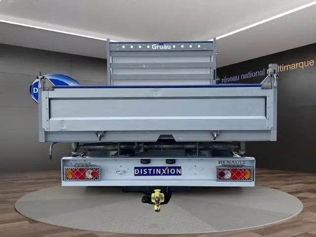 Vue arrière d'un Renault Master blanc double cabine avec benne grise et attelage visible en intérieur showroom.