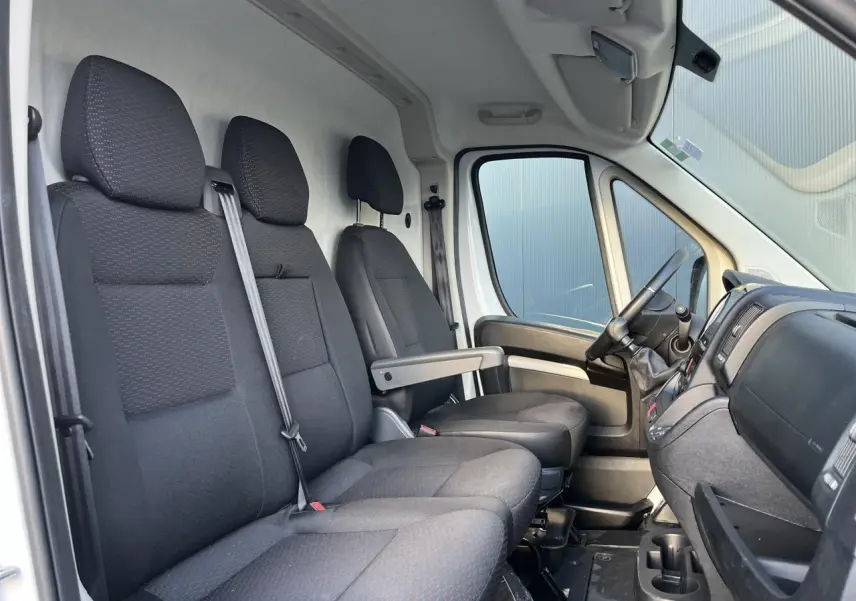 Vue intérieure côté conducteur de l'Opel Movano Fourgon 2024, sièges noirs et tableau de bord avec volant et levier de vitesses.