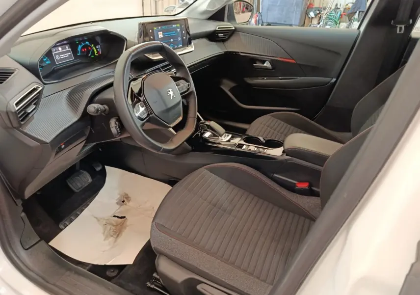Intérieur avant droit de la Peugeot 208 électrique blanche, volant cuir, tableau de bord numérique et écran tactile central.